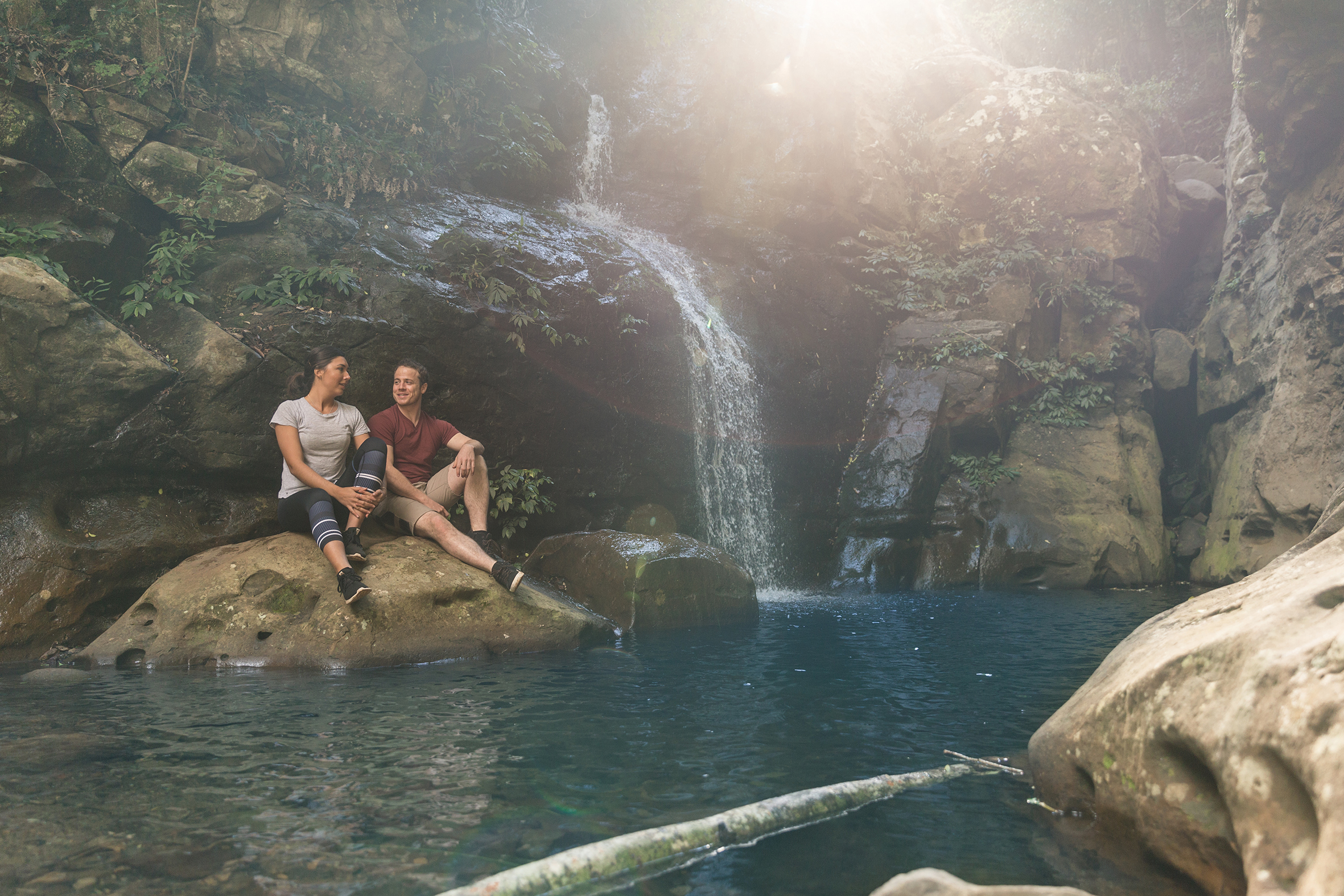 Two people sitting on a rock at the base of the Cascades Waterfall