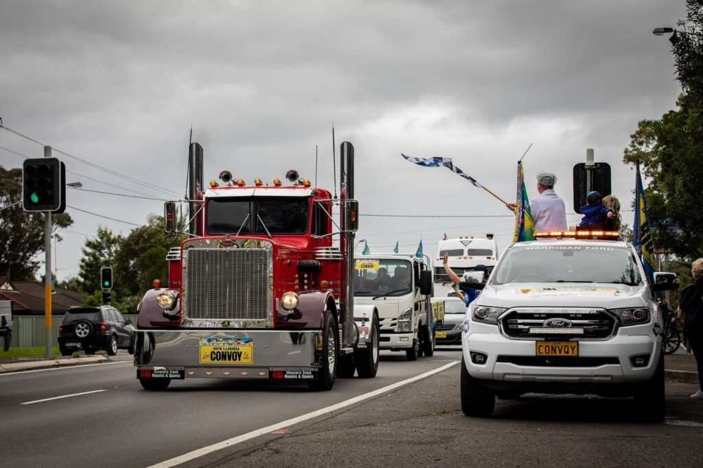 Convoy lead truck driving along road. Man waving finish line flag from back of truck.