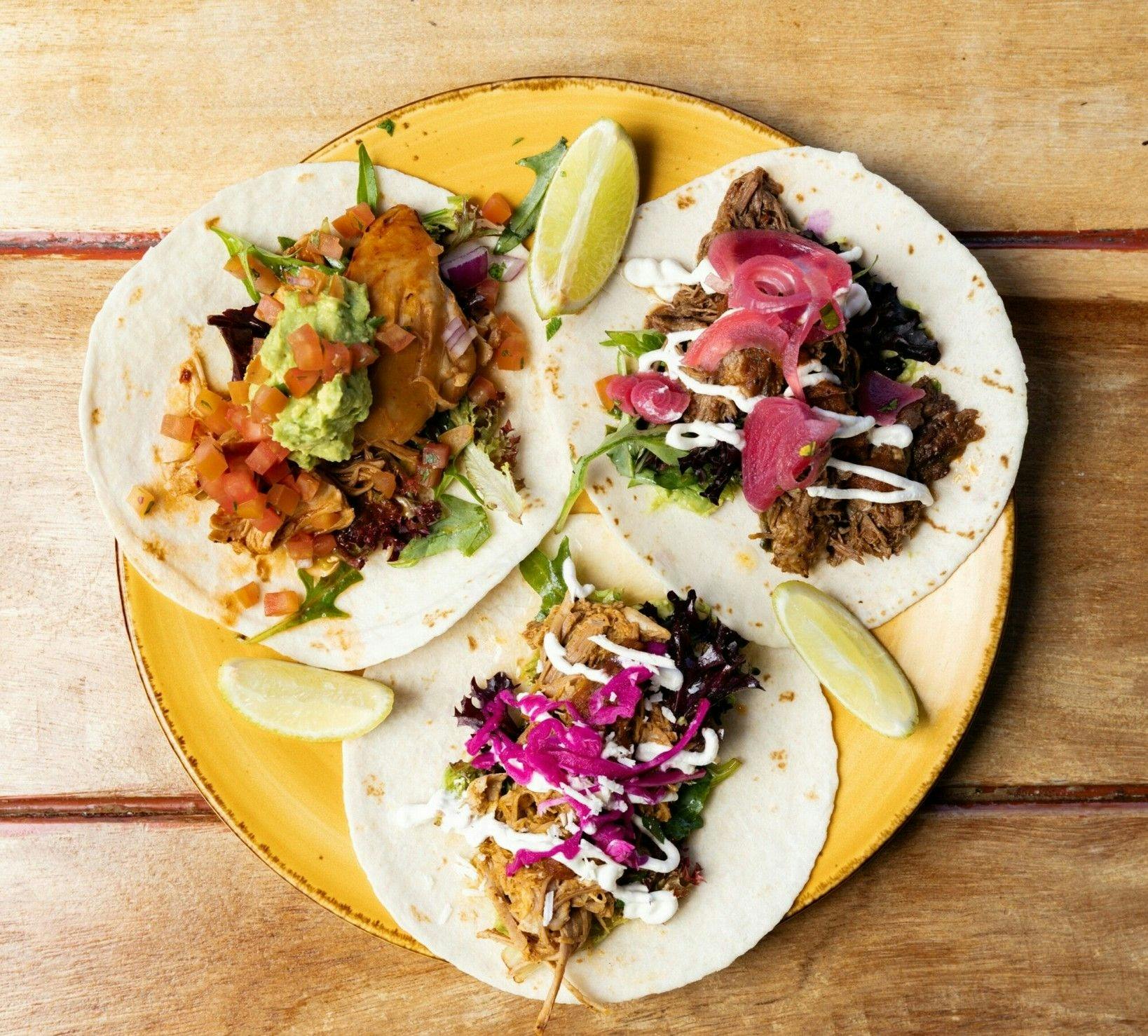 Three different types of tacos on a plate with lime pieces at El Corazon Mexican Shellharbour City