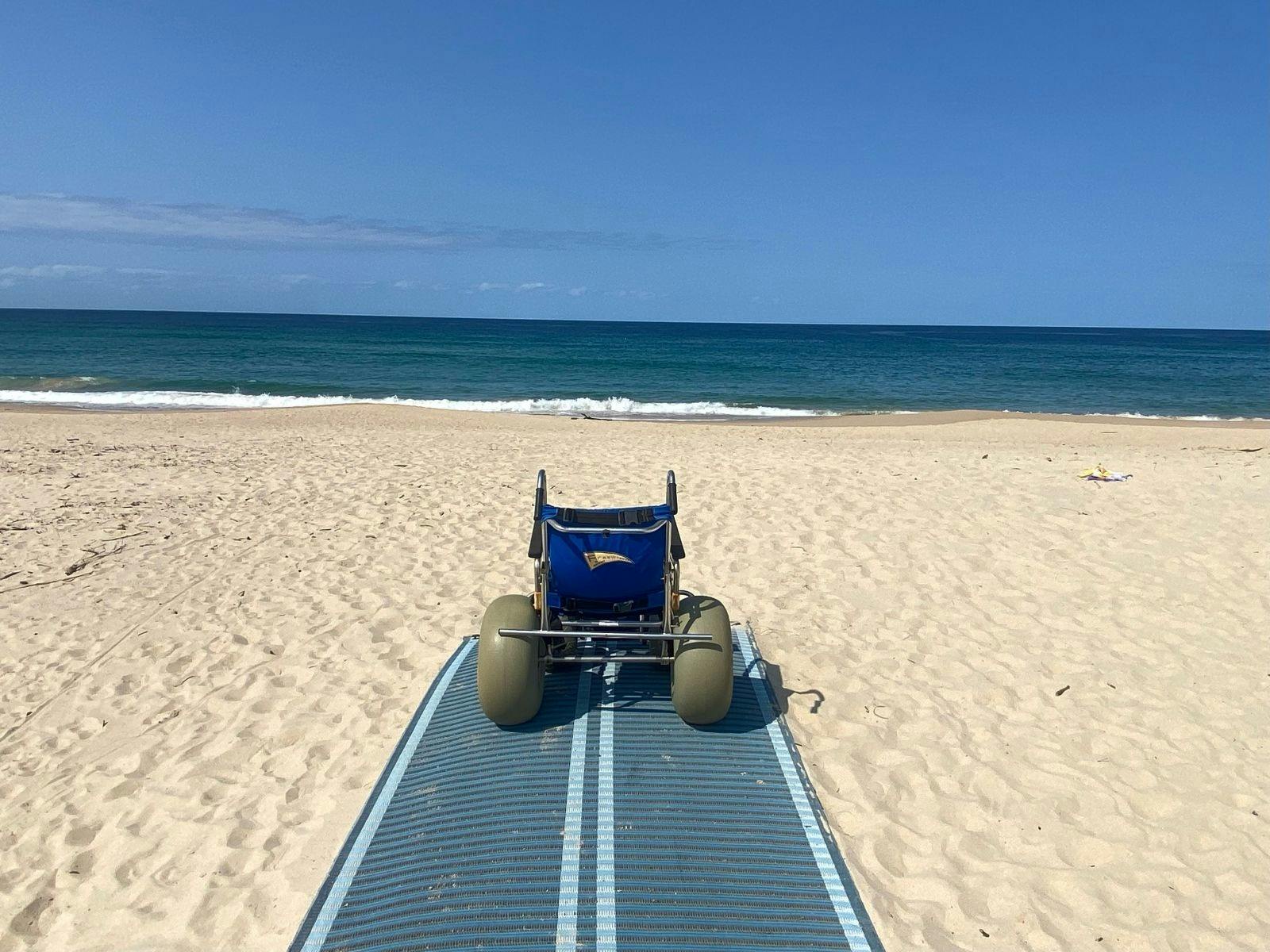 Sand Wheel Chair sitting on a sand matt on the beach with ocean in the distance  at Shellharbour