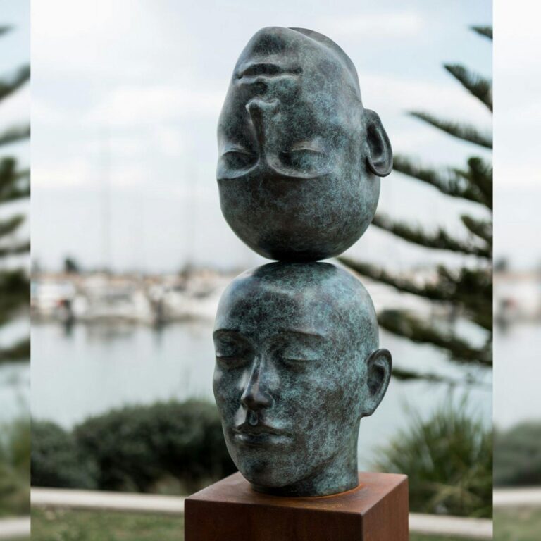 Sculpture of two heads, one upside down ontop of the other. Both made of metal.