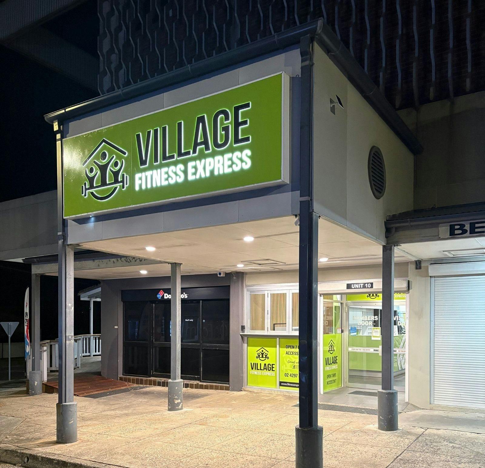 Village Fitness Express entry at night with illuminated sign