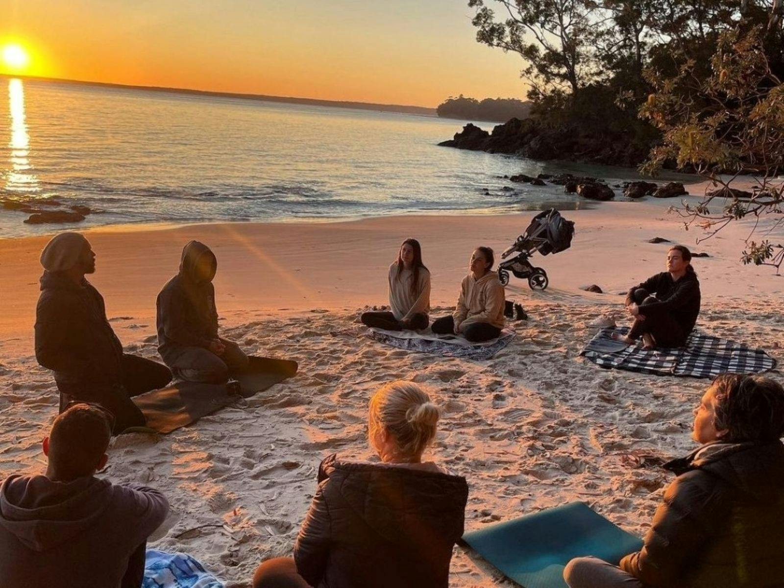 A group of people sitting in a circle on the beach doing breathwork training