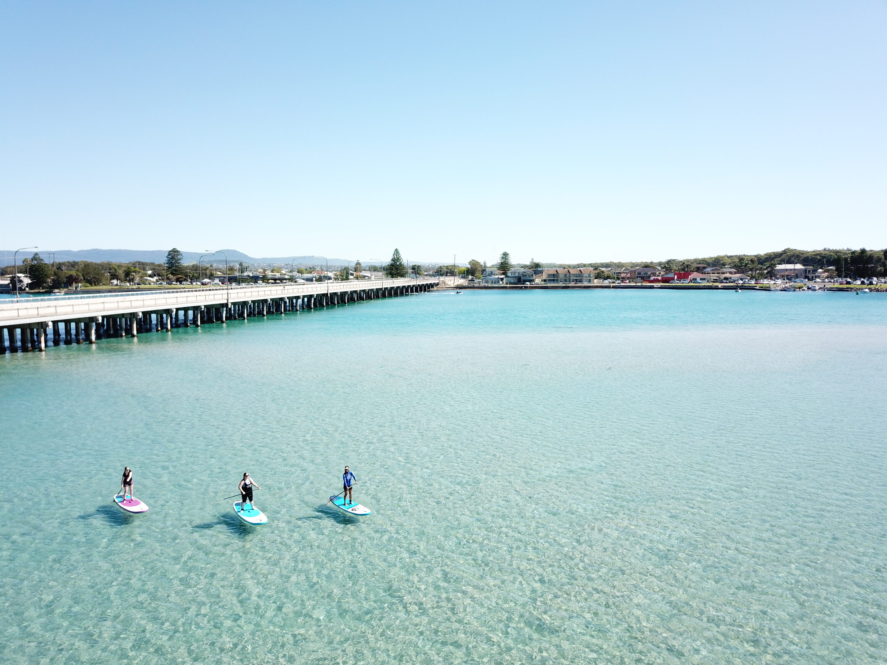 Three people stand up paddle boarding on the vast expanse of Lake illawarra