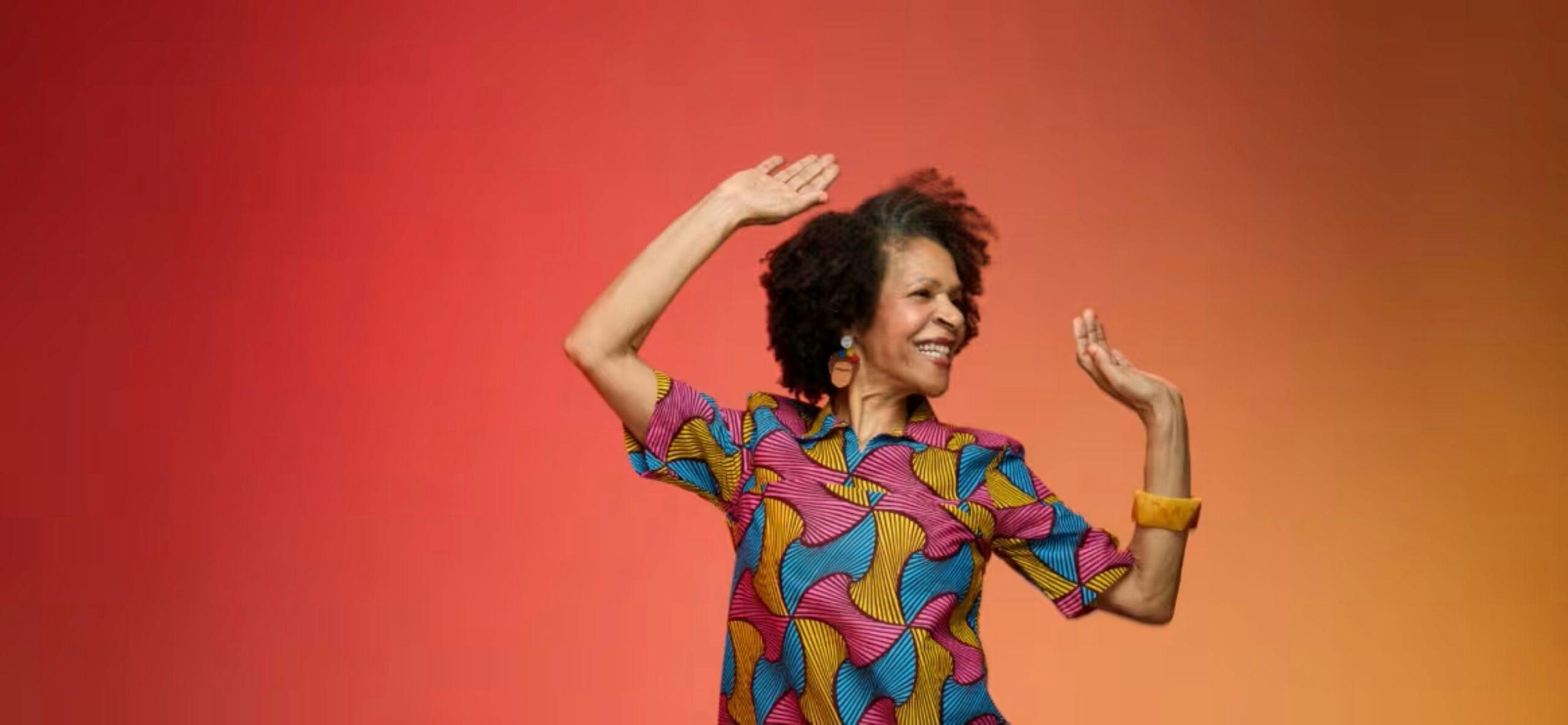 Lady with dark hair and colourful dress dancing with an orange background.