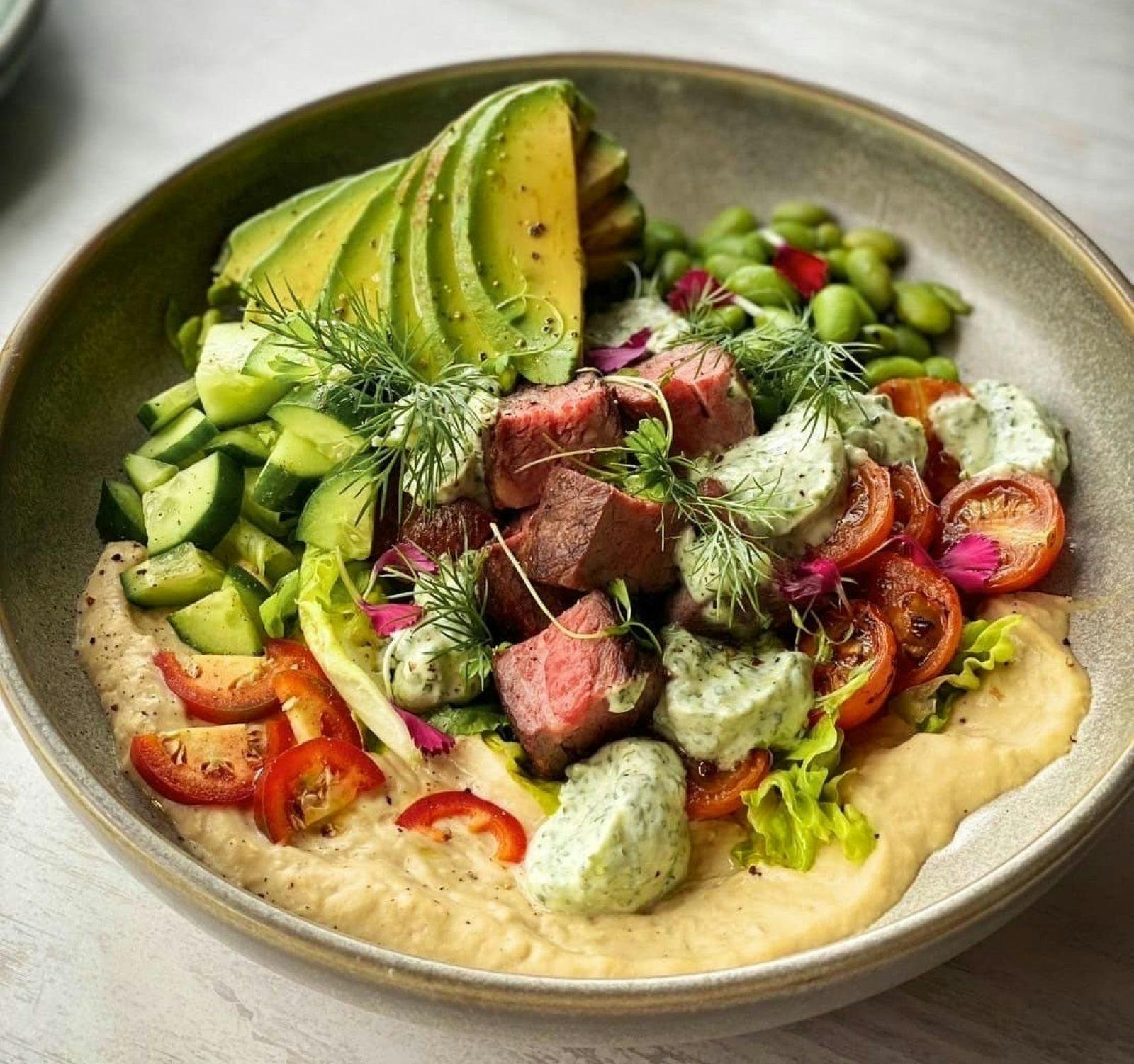 Beef bowl with avocado and fresh vegetables on a bed of hummus