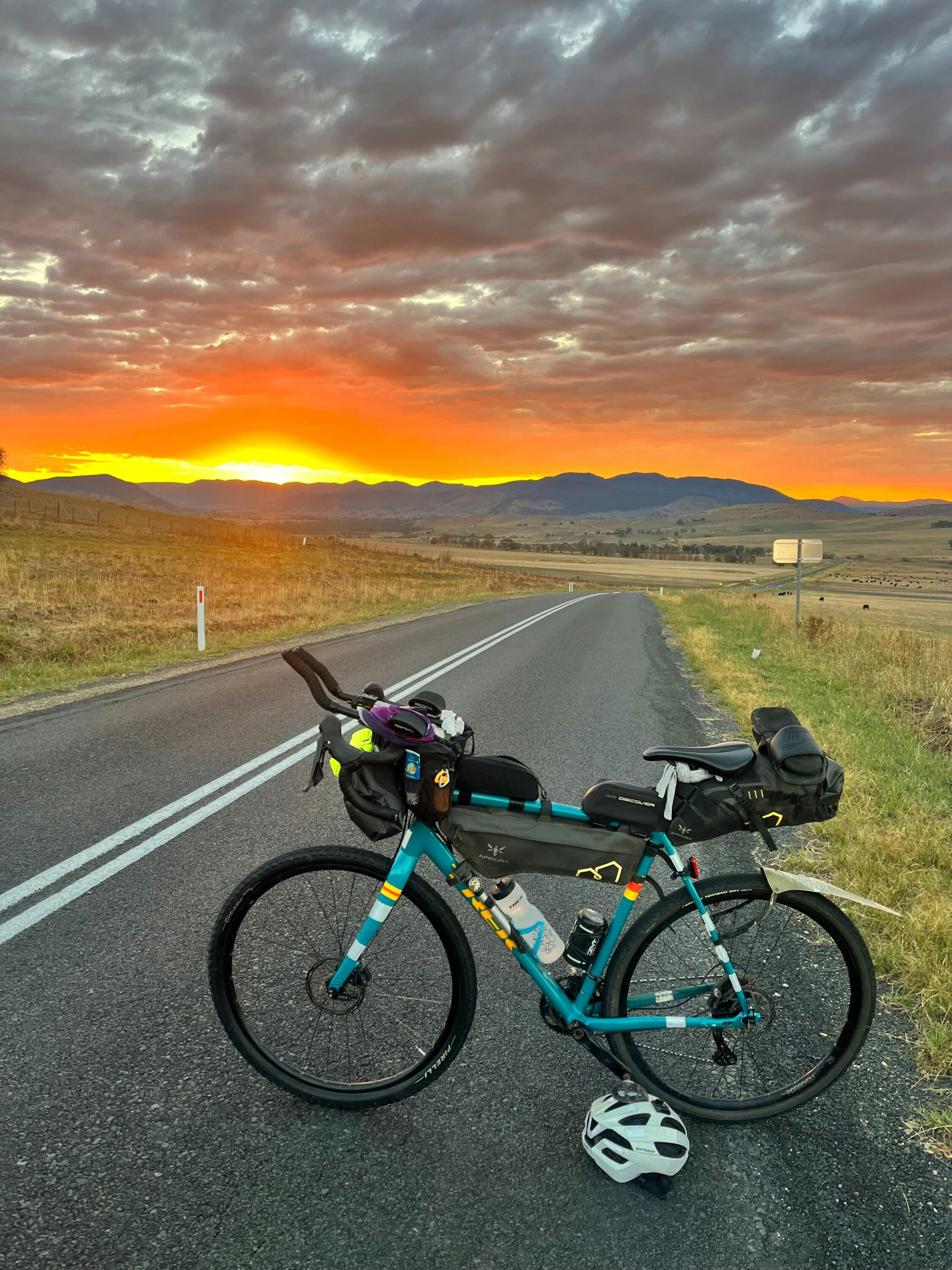A bicycle on a deserted highway with the sun setting over the hills in the background